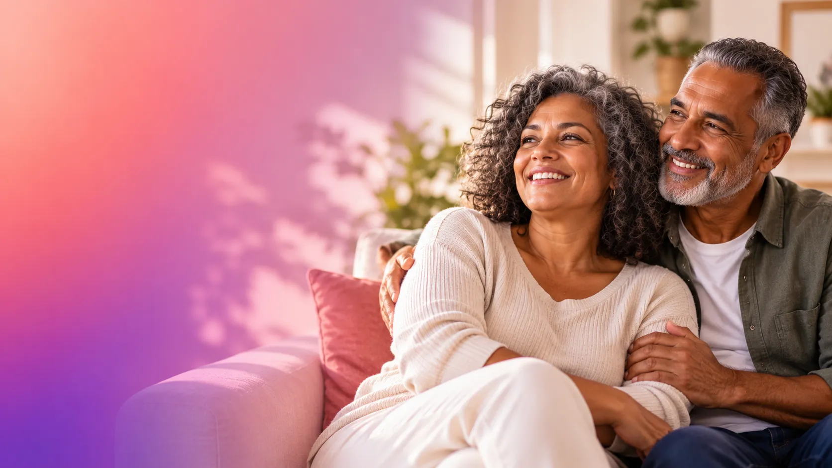 Casal brasileiro com mais de 60 anos, sorridente e abraçado no sofá, em um ambiente acolhedor, com tons de rosa e roxo ao fundo.